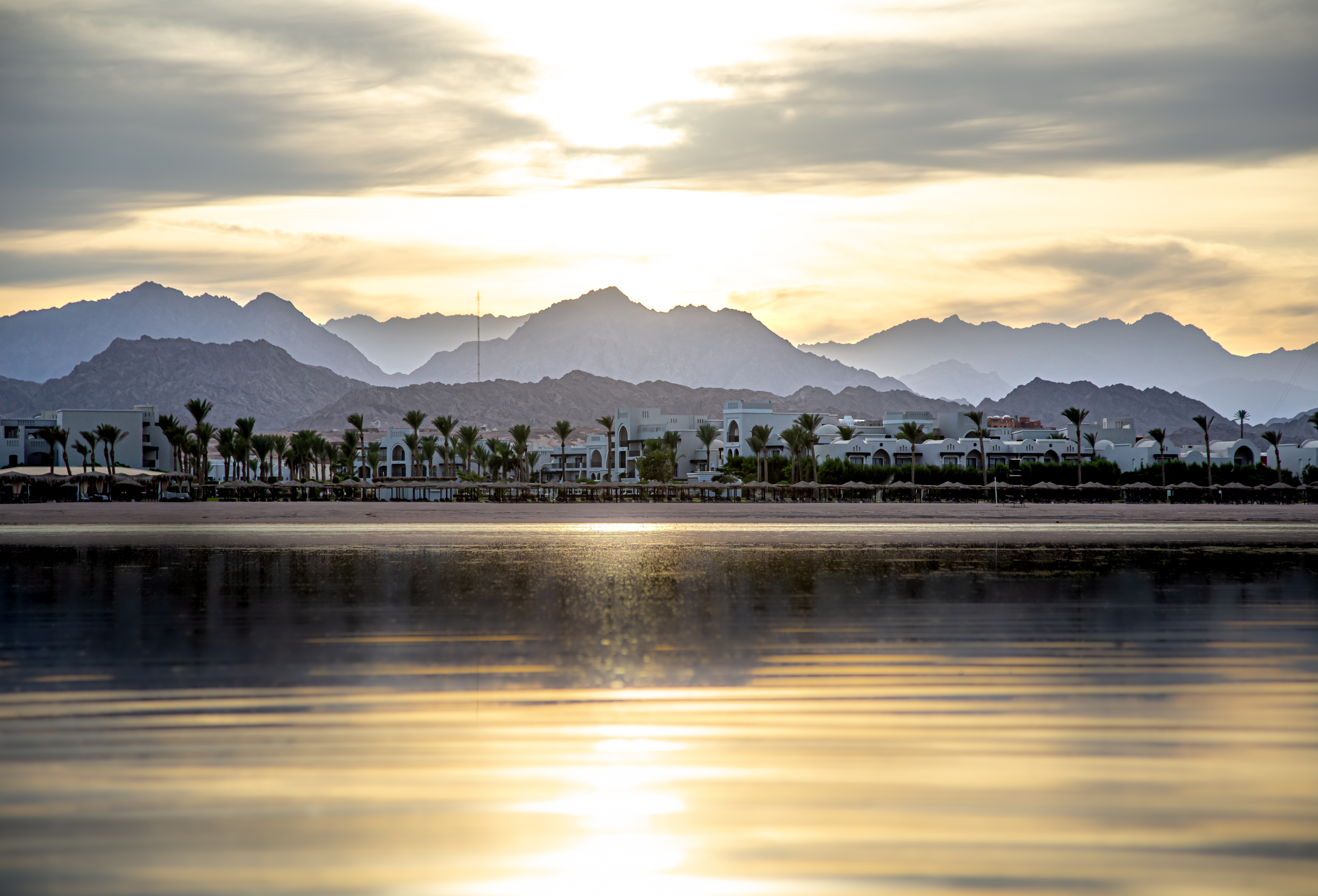 The landscape sky is reflected in the sea in the setting light. City coastline with mountains on the horizon.